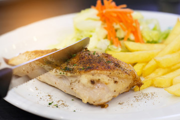 Chicken steak with vegetable and french fries on a white plate on black wooden background (focus steak).