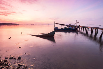 Fototapeta na wymiar Sunrise by the shore with silhouette of broken boat