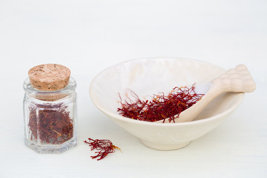 Saffron pistil in spoon and in glass jar on white background