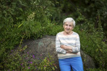 An elderly woman stands in a green forest.