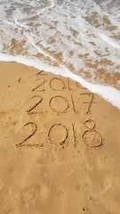 Happy New Years 2017 and 2018 handwritten on sand with a wave coming to erase 2016