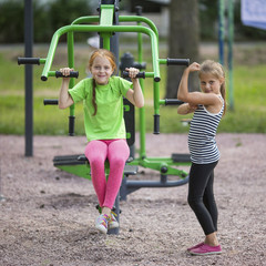 Fototapeta na wymiar Little cute girls doing exercises at public sports equipment..