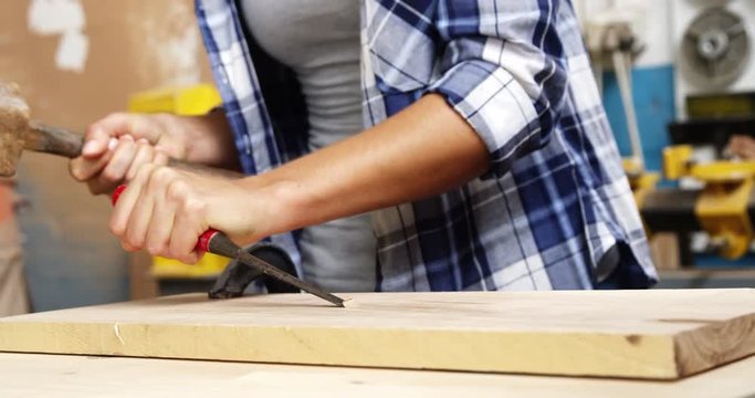 Focus on carpenter using hammer and chisel on a wooden plank