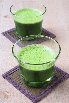 Close up of a glass of mixed green vegetable juice on a wooden table.