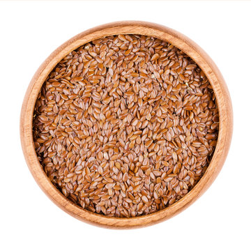 Brown flaxseeds in a wooden bowl on white background. Also known as common flax or linseed. Raw edible food. Linum usitatissimum of the Linaceae family. Isolated, macro photo and close up from above.