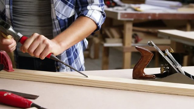 Focus on carpenter using hammer and chisel on wooden plank