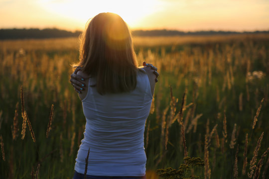 Young woman hugging herself in a wheat field. He looks into the