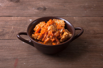 Fish marinated with carrots in a brown ceramic bowl on old woode
