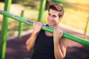 Fitness man doing stomach workouts on horizontal bar outdoors