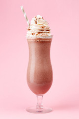 Glass of cold chocolate milkshake with whipped cream on pink bac