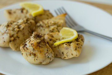 Baked chicken breast with thyme, pepper and lemon on a white classic plate, fork on the background