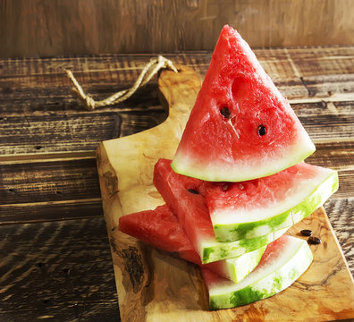 Triangular pieces of a water melon on a kitchen board and a wooden background