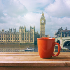 Red coffee cup on wooden table over London Big Ben landmark background