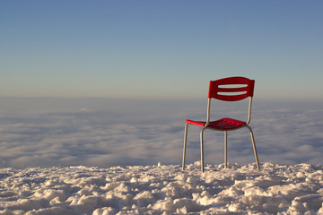 Verlassener roter Stuhl auf weißem schneebedecktem Berg Gipfel mit Aussicht auf Wolken Meer.