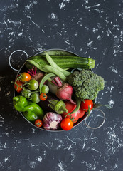 Assortment of fresh vegetables - broccoli, zucchini, tomatoes, peppers, green beans, beets, garlic in a metal basket on dark background