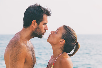 Attractive young couple sharing a kiss with a bubble gum on the beach
