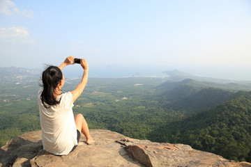Naklejka na ściany i meble young asian woman taking photo with smart phone at mountain peak cliff
