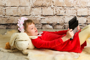Little Girl with Tablet Computer on White Wall Background. Education works on the tablet for children. Children and computer technology.