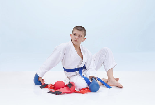On a light background karate athlete sits near a karate outfit