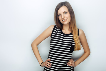 Obraz premium Portrait of happy young beautiful woman in striped shirt posing with hands on hips for model tests against studio background