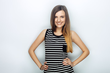 Portrait of happy young beautiful woman in striped shirt posing with hands on hips for model tests against studio background