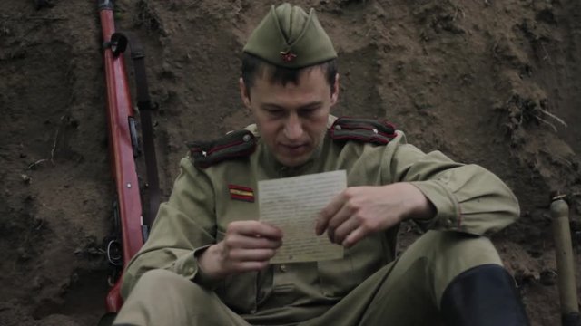 Soviet soldier sits in trench and reads a letter from home. World War II.