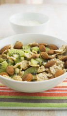 Whole grain cereal with kiwi and almond in white bowl and yogurt