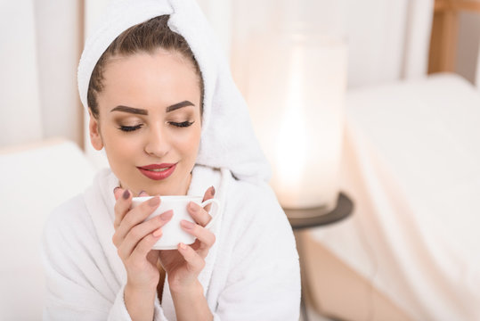 Cheerful girl drinking beverage on bed at salon
