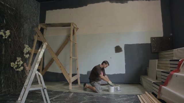 Young builder carefully mixes up gray paint in white plastic pail.