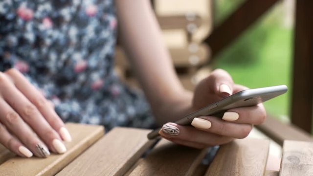 Closeup of young woman hands scrolling pictures phone. surfing internet. outdoors