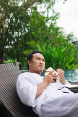 Fototapeta premium man drinking a coconut juice on deck chairs next to a swimming pool 