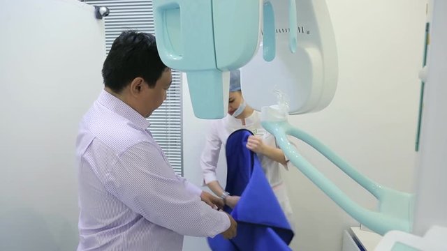 Nurse helps patient to wear a protective apron of lead to protect from radiation during use of dental scanner.
