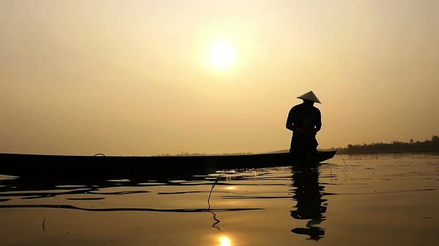 Silhouette of traditional fishermen throwing net fishing in the lake at sunrise time