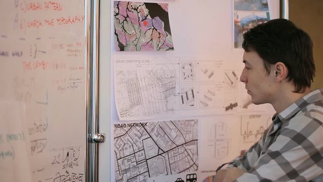Young professional at urban development considers future areas given for construction, standing next to map and plans of area.