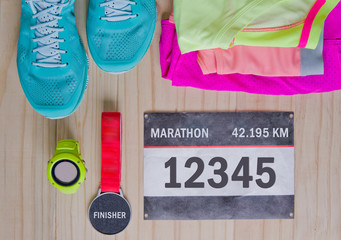 Top view of outfit for runner on wooden background: bib number, finisher medal, gps watch, running...