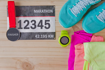 Top view of outfit for runner on wooden background: bib number, finisher medal, gps watch, running...