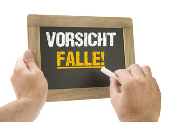 Hand schreibt Vorsicht Falle! auf Kreidetafel