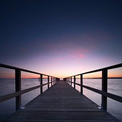 Fototapeta na wymiar Long Wooden Pier into a Lake at Sunset, perfect symmetry