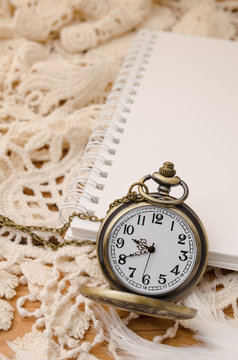 Vintage pocket watch with blank note book on lace background
