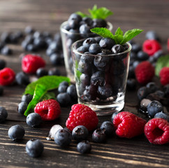 Blueberries, raspberries and mint at black wooden table.