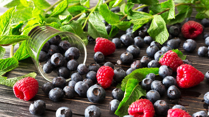 Blueberries, raspberries and mint at black wooden table.