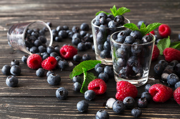 Blueberries, raspberries and mint at black wooden table.
