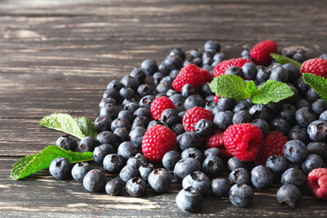 Blueberries, raspberries and mint at black wooden table.