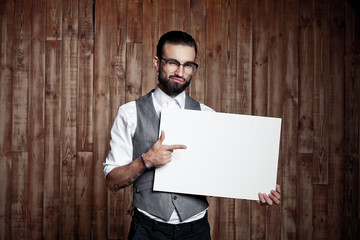 Stylish guy with a white sign for text on wooden background, rea