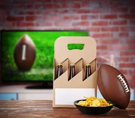Foto op Canvas Six pack of beer, snack and ball on wooden table in front of television show of football. Watching football match at home. © Africa Studio