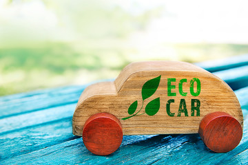 Wooden toy car with text eco car on bench outdoor. Transport and ecology concept.