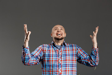 Naklejka premium Portrait of handsome middle-aged man screaming up lifting hands in plaid shirt over grey background.