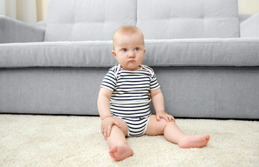 Adorable little baby sitting on light carpet