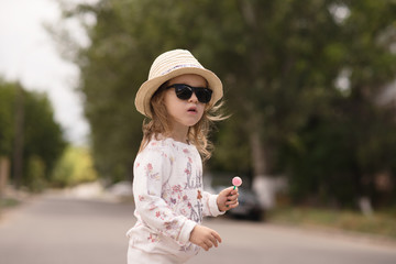 Portrait of stylish little girl in hat and sunglasses with lollipop