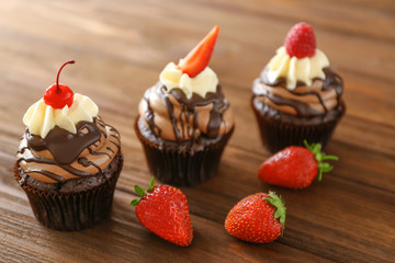Tasty chocolate cupcakes with berries on wooden background
